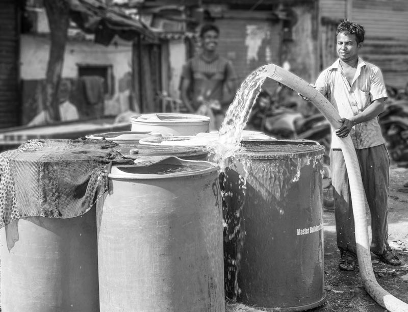 Big  plastic drums being filled with drinking water from tanker. The stored water is used cautiously over several days – Mumbai, Maharashtra